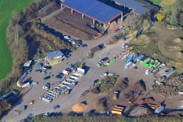 Luftbild der Grnkompostierungsanlage Kssaberg mit Recyclinghof. Vorne links  befindet der Recyclinghof mit den Boxen und den Altkleidercontainern. Dahinter ist das Betriebsgebude zu sehen. Im vorderen rechten Bereich befinden sich Hgel mit verschiedenen Materialien wie Erde, Sand, Holzschnitzel etc., die fr den Gartenbau bentigt werden. Im Hintergrund links ist der Abgabeort fr den Grnschnitt zu sehen, sowie Hallen mit dem zum Teil bereits aufbereiteten Kompost.